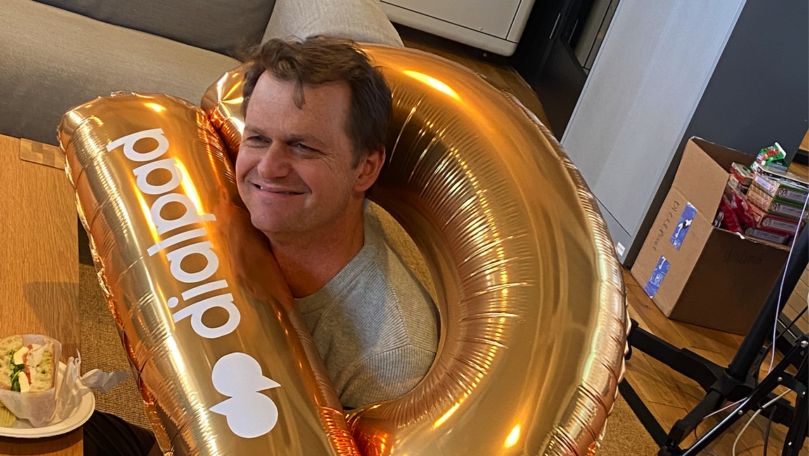 A Dialpad employee wears a large, golden balloon with the Dialpad logo around his neck. 