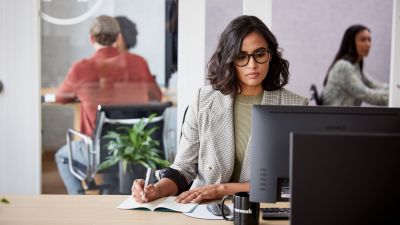 Woman looking at a screen and taking notes.