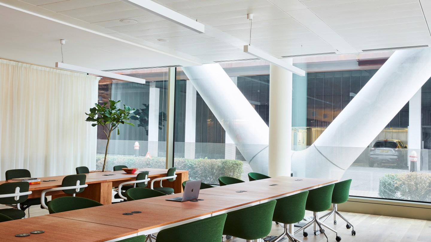 shared WeWork workspace with tables, desks, and floor-to-ceiling windows