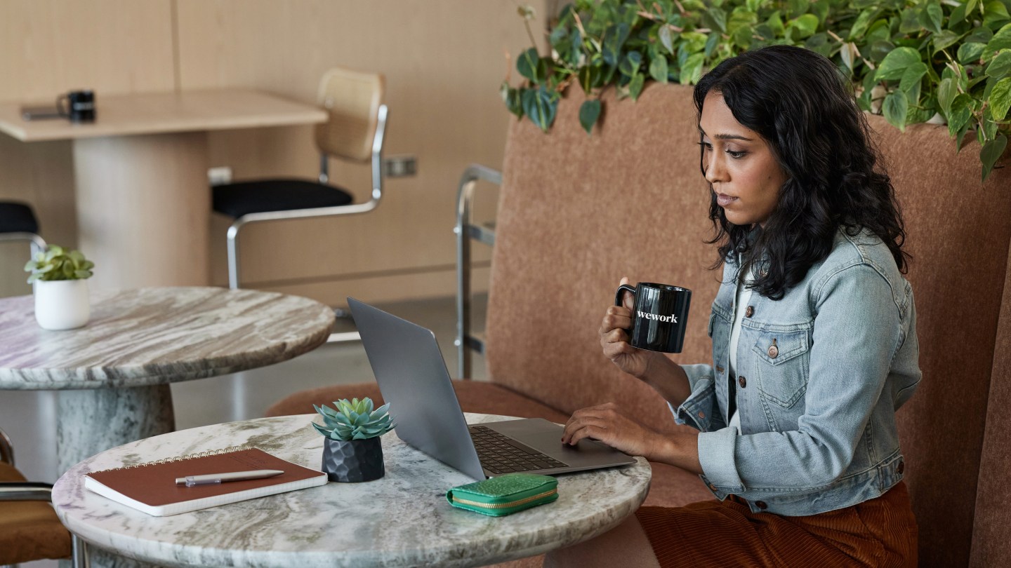 woman working on laptop while holding a WeWork mug