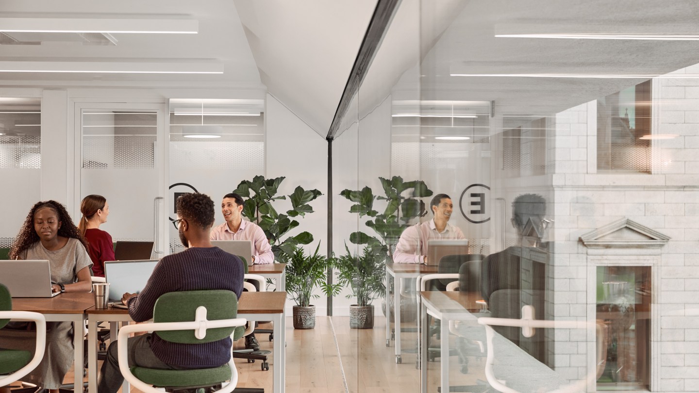 WeWork members in a shared workspace with glass windows