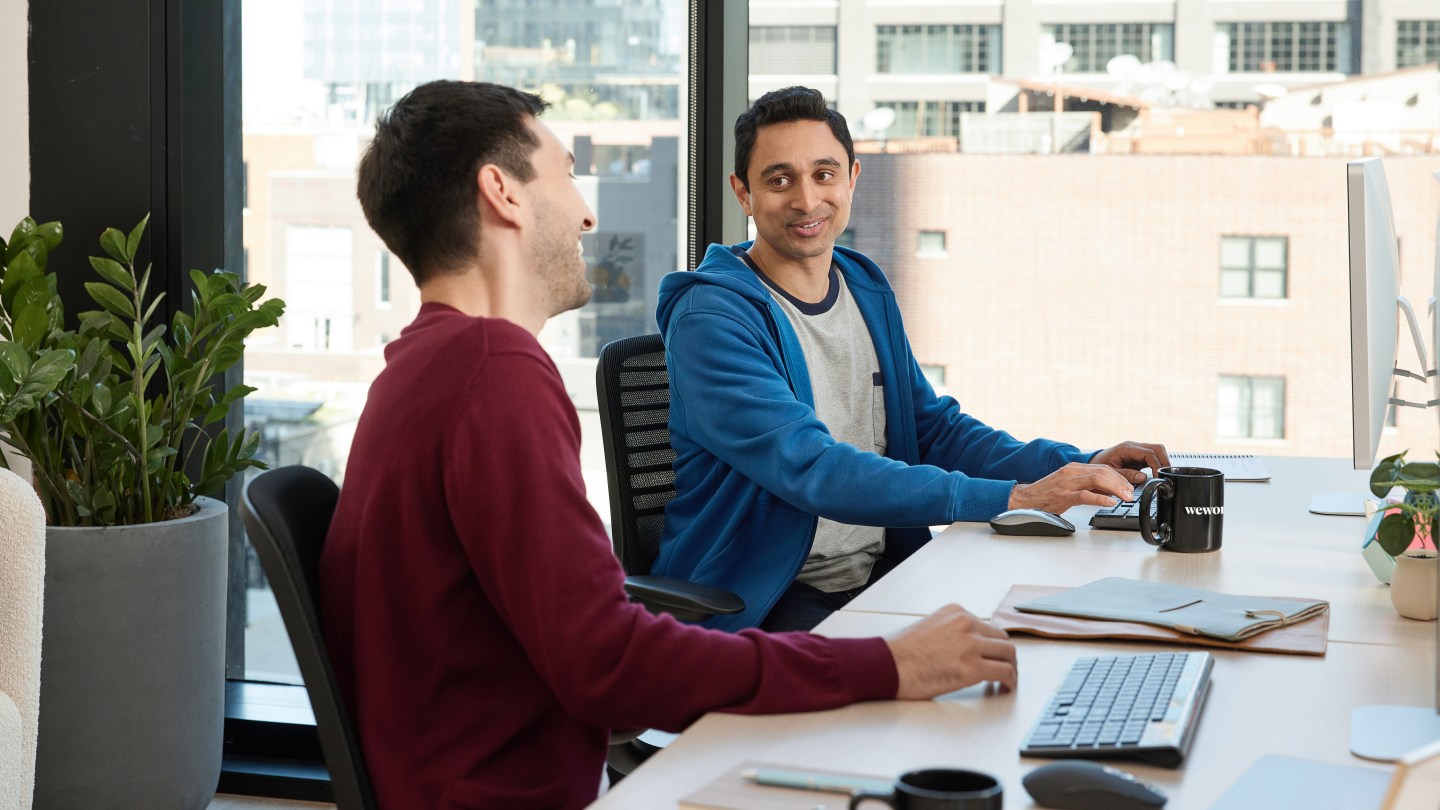 two people socializing and having a laugh at WeWork desks