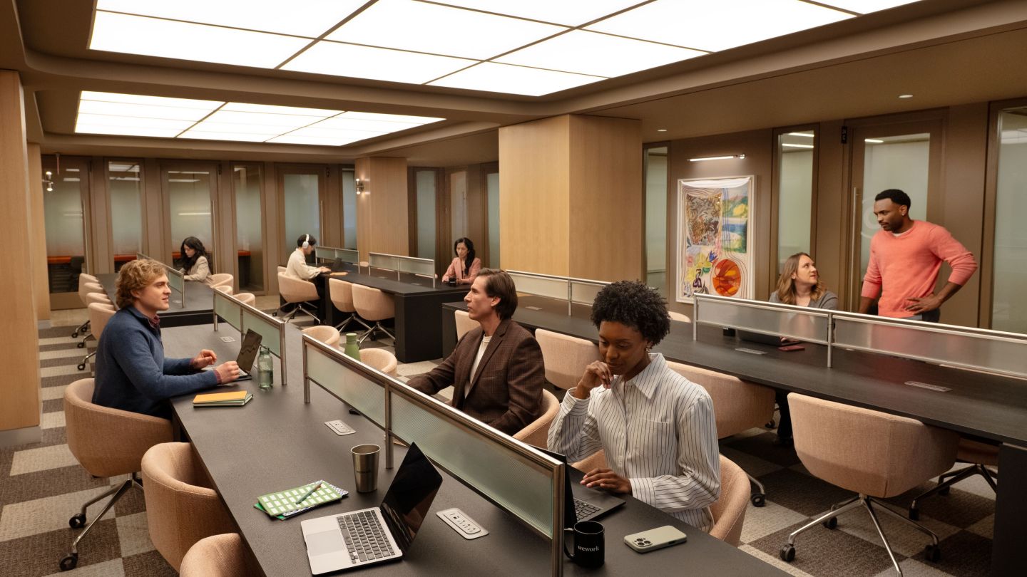 People working and chatting over their screens in the same area of a coworking space. 