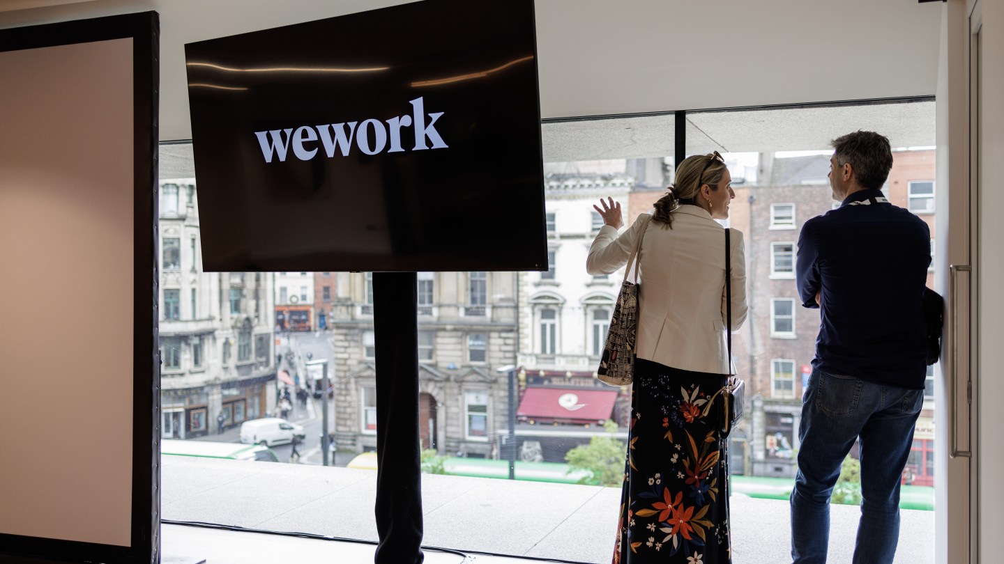 Two people in an office with city views and a screen showing the WeWork logo
