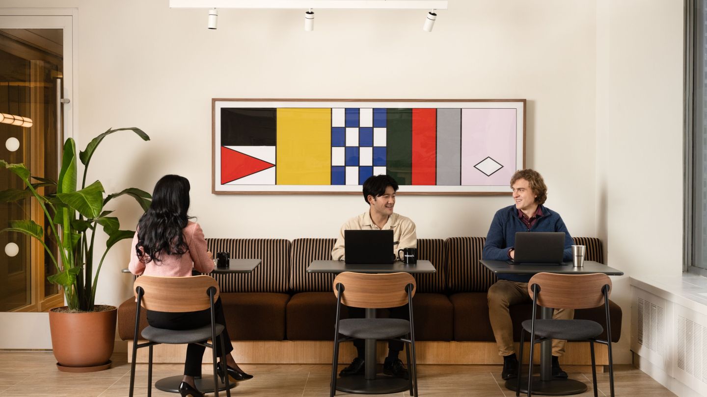 Three people sitting at separate tables in a common area but glancing towards each other.